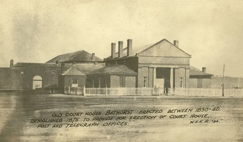 Photograph of a columned court house with tall chimneys and a picket fence, with a handwritten note along the foot of the print.